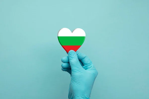 Tangan mengenakan sarung tangan bedah pelindung memegang bendera jantung Bulgaria — Stok Foto