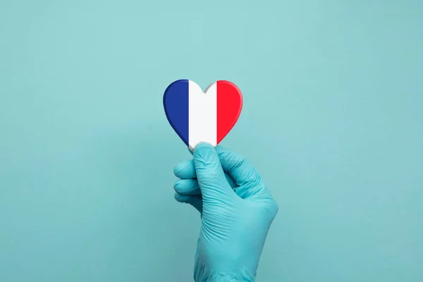 Ruce nosí ochranné chirurgické rukavice držící srdce francouzské vlajky — Stock fotografie
