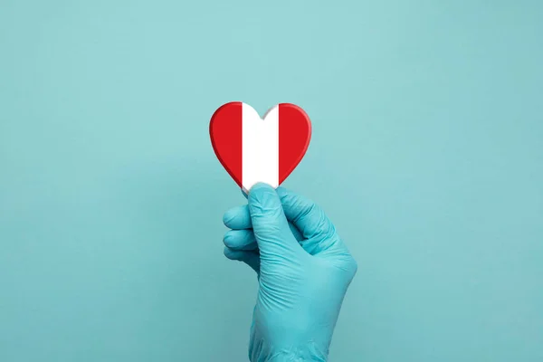 Manos con guantes quirúrgicos protectores que sostienen el corazón de la bandera Perú — Foto de Stock