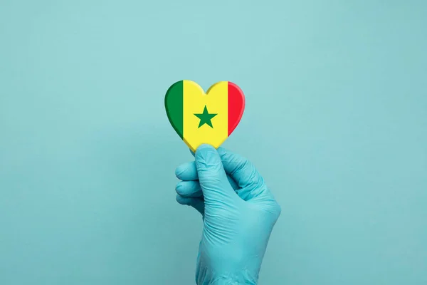 Manos con guantes quirúrgicos protectores que sostienen el corazón de Senegal — Foto de Stock