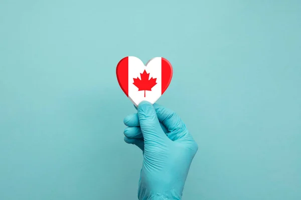 Hands wearing protective surgical gloves holding Canada flag heart — Stock Photo, Image