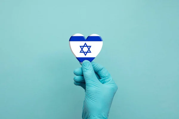 Χέρια που φορούν προστατευτικά χειρουργικά γάντια κρατώντας την καρδιά σημαία Ισραήλ — Φωτογραφία Αρχείου
