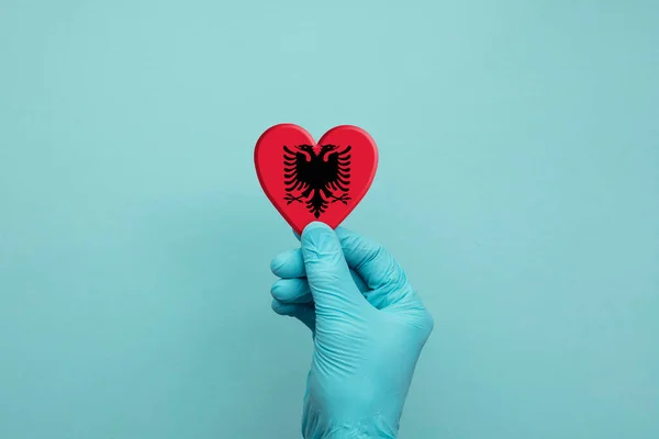 Ruce nosí ochranné chirurgické rukavice držící srdce albanické vlajky — Stock fotografie