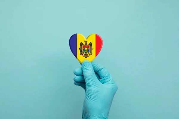 Hände mit schützenden OP-Handschuhen, die ein Herz mit moldawischer Flagge tragen — Stockfoto