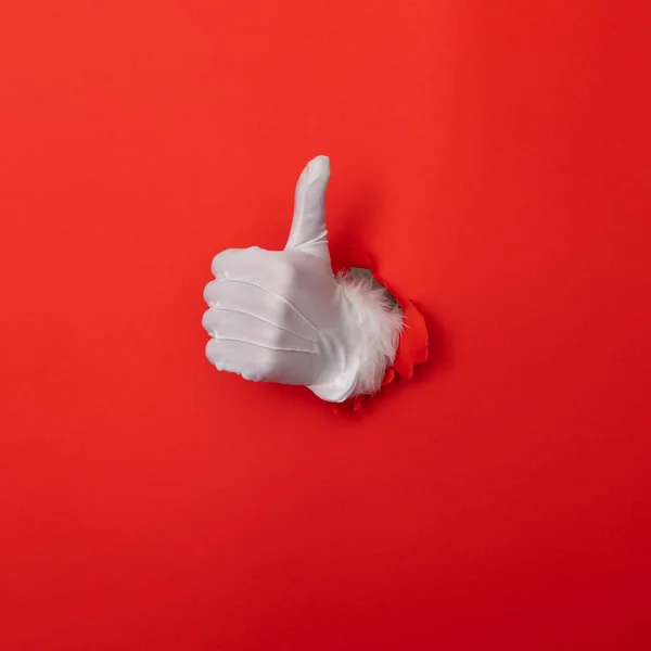 Santa Claus hand thumbs up through a hole in red paper background — Stockfoto