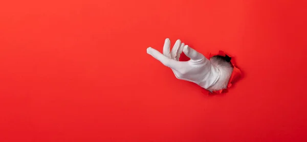 Santa Claus hand wearing white glove through a hole in red paper background — Stockfoto