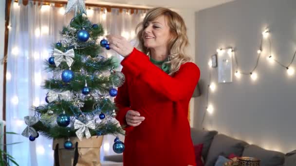 Mooie Blonde Vrouw Een Rode Trui Zetten Decoratie Kerstboom Woonkamer — Stockvideo