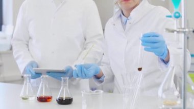 Laboratuvarda kenevir CBD, CBDA yağları ve tabletle çalışan iki bilim adamı. Lateks eldiven, cam tüpler ve erlenmeyer şişeleri kullanıyorlar. Esrar tohumlarından alınan sağlık hizmetleri eczanesi.