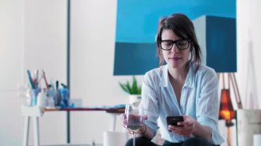 Genç bir ressam stüdyosunda oturuyor ve cep telefonundan bir şeyler okuyor. Ressam gözlük takıyor ve elinde bir bardak beyaz şarap tutarken, resim malzemesi arka planda onun etrafında görülebilir..