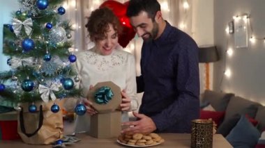 Yakışıklı bir adam Noel ağacının yanında hediye ve kalp şeklinde bir balonla kız arkadaşına sürpriz yapıyor.
