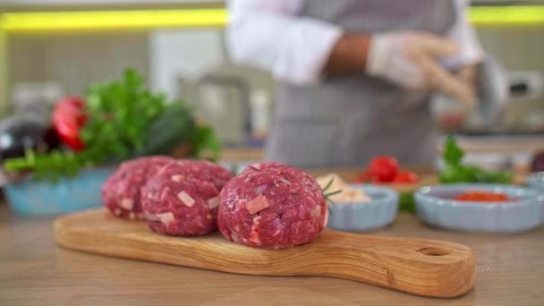 キッチンの木の板にプレスでハンバーガー用の肉を形作るシェフのクローズアップ 作業面の周りには様々なスパイス 小さなキッチンボウルがあります — ストック動画