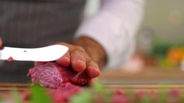 Ahşap mutfak tahtasının hazırlık safhasında şefin ellerinin carpaccio etini ince parçalara ayırması. Çalışma yüzeyinde çeşitli küçük mutfak kaseleri ve sebzeler görülebilir..