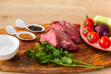 Mutfak tahtasındaki çiğ etin yakın plan görüntüsü hazırlanmaya hazır. Çevrede çeşitli sebzeleri meze ve baharatlı küçük mutfak kaseleri olarak görebilirsiniz..