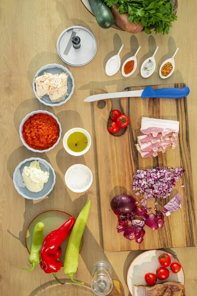 Top view of kitchen work surface with bacon, knife and groceries such as spices and vegetables on a wooden board.