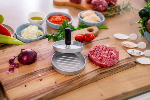 Burger presi ahşap kesim tahtasına ve sebze, baharat ve mutfak kapları gibi mutfak tezgahlarının etrafına yerleştirilmiş kâselerle birlikte mutfak yüzeyine konur..