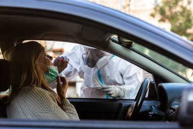 Otomobil sürücüsü COVID-19 testi yapıyor. Kadın hastadan araba camından geniz örneği alıyor. Coronavirus için PCR testi yapıyor..