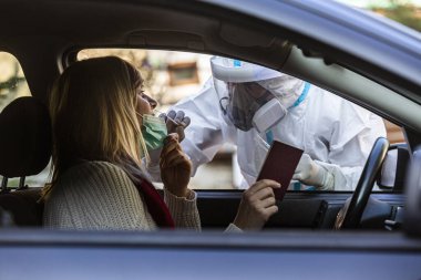 Otomobil sürücüsü COVID 19 testi yapıyor. Kadın hastadan, araba camından burun örneği alıyor. PCR teşhisi koyuyor. Pasaportları var..