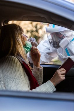 Otomobil sürücüsü COVID 19 testi yapıyor. Kadın hastadan, araba camından burun örneği alıyor. PCR teşhisi koyuyor. Pasaportları var..