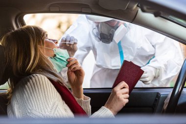Otomobil sürücüsü COVID 19 testi yapıyor. Kadın hastadan, araba camından burun örneği alıyor. PCR teşhisi koyuyor. Pasaportları var..