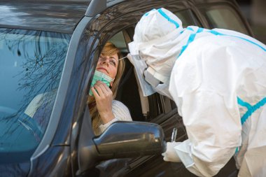 Otomobil sürücüsü COVID-19 testi yapıyor. Kadın hastadan araba camından geniz örneği alıyor. Coronavirus için PCR testi yapıyor..