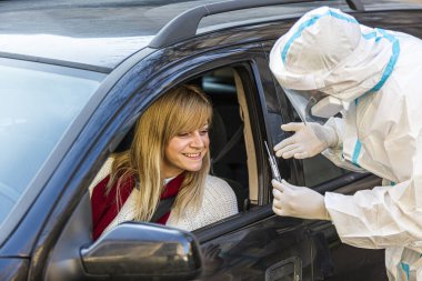 Arabada oturan bir kadın, tıbbi çalışanın COVID-19 testi yapmasını bekliyor. Araba camından burun temizleme örneği alıyor. Coronavirus için PCR testi yapıyor..