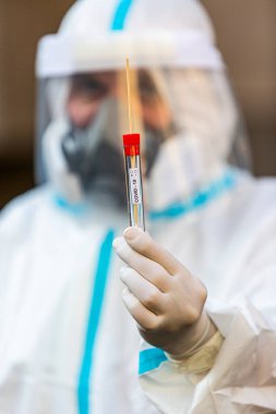 COVID-19 testi yapan bir tıp çalışanı, hastadan alınan burun temizleme örneği için. Koronavirüs için PCR teşhisi, PPE 'deki doktor test kiti tutuyor..