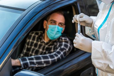 Arabada oturan bir adam, tıbbi çalışanın COVID-19 testi yapmasını bekliyor. Arabanın camından burun temizleme örneği alıyor. Coronavirus için PCR testi yapıyor..