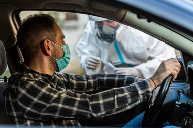 Arabada oturan bir adam, tıbbi çalışanın COVID-19 testi yapmasını bekliyor. Arabanın camından burun temizleme örneği alıyor. Coronavirus için PCR testi yapıyor..