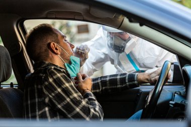 Otomobil sürücüsü COVID-19 testi yapıyor. Erkek hastadan araba camından geniz örneği alıyor. Coronavirus için PCR testi yapıyor..
