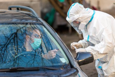 Otomobil sürücüsü COVID 19 testi yapıyor, erkek hastadan araba camından burun örneği alıyor, PCR teşhisi koyuyor, PE 'de elinde test kiti olan bir doktor. Pasaportları var..