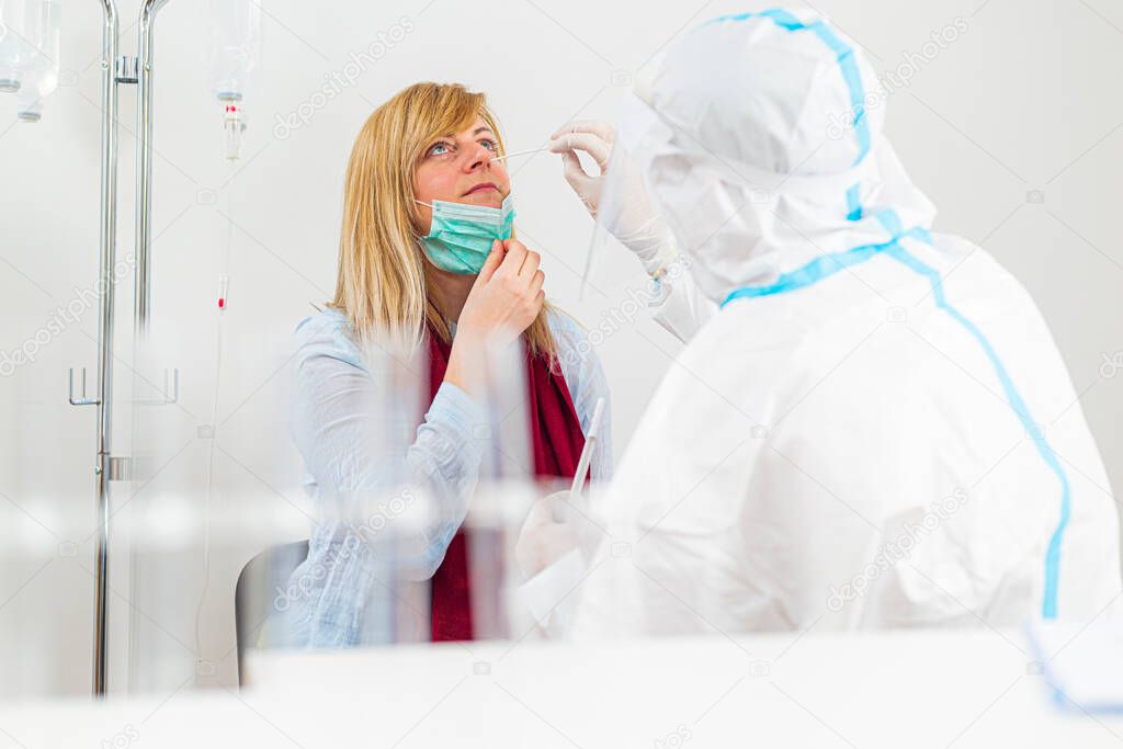 Medical worker performing COVID-19 test, taking nasal swab sample from female patient in hospital lab, PCR diagnostic for Coronavirus, doctor in PPE using test kit.