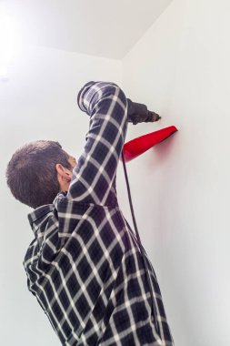 Rafları yerleştirmek için duvarlara delik açan bir marangoz. Bir elinde matkap, diğer elinde havan topunun tozunu toplamak için küçük bir spatula tutuyor..