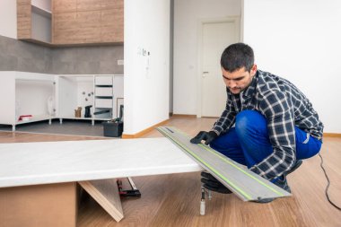 Bir marangoz boş bir odanın zeminine klempi yerleştirir. Mutfağın çalışma yüzeyi için tasarlanmış bir çalışma tahtasına..