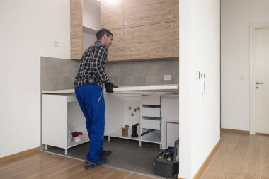 Marangoz mutfağın çalışma yüzeyini, duvarda asılı elementlerle birlikte neredeyse bitmiş mutfağa yerleştirir..