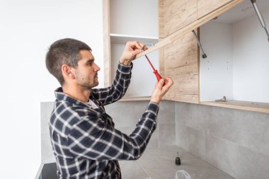 Marangoz destek veren mutfak elementinin kapısına bir tornavida yerleştirir ve vidaları yerleştirir..