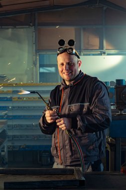 Tamirci, otomatik kaynak aletini işe hazırlarken meslektaşı arkada öğütme işiyle uğraşırken fark edilebilir..