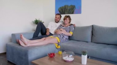 Genç ve kucaklayıcı bir çift oturma odasındaki kanepede yatıyor. Mutlular, televizyon izliyorlar, adam bir elini kadının hamile karnına koyuyor..