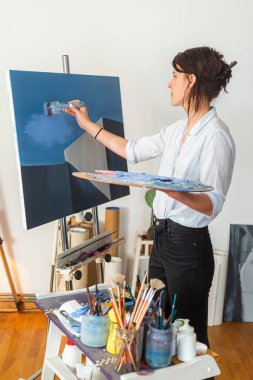 Genç, gülümseyen bir ressam kendi stüdyosundaki tuvale boya sürüyor. Etrafında resim yapmak için eşlik eden diğer malzemeler de görülebiliyordu. Bazı fotoğraflarda, bir elinde bir palet boya tutarken, diğer elinde de acı ile boyayı sürüyor.