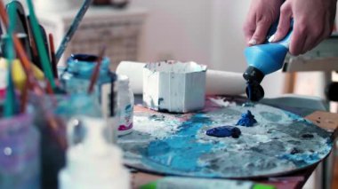 Stüdyodaki bir palette ressamın elini kapatıyoruz. Paletin etrafında kavanozlarda resim yapmak için bir sürü fırça var..