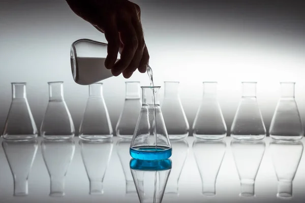 反射面にガラス器具を使用した科学用エルレメリアフラスコに白色の液体を注ぐ手 — ストック写真