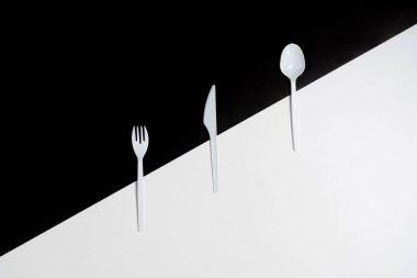 Çapraz bölünmüş siyah beyaz arka planda plastik çatal, bıçak ve kaşık..