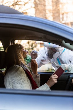 Otomobil sürücüsü COVID 19 testi yapıyor. Kadın hastadan, araba camından burun örneği alıyor. PCR teşhisi koyuyor. Pasaportları var..