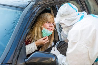 Otomobil sürücüsü COVID-19 testi yapıyor. Kadın hastadan araba camından geniz örneği alıyor. Coronavirus için PCR testi yapıyor..