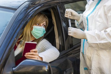 Otomobil sürücüsü COVID 19 testi yapıyor. Kadın hastadan, araba camından burun örneği alıyor. PCR teşhisi koyuyor. Pasaportları var..
