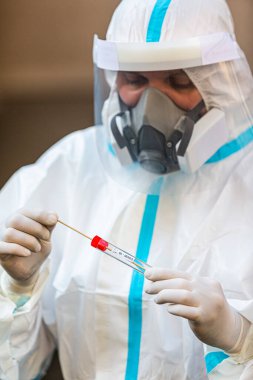 COVID-19 testi yapan bir tıp çalışanı, hastadan alınan burun temizleme örneği için. Koronavirüs için PCR teşhisi, PPE 'deki doktor test kiti tutuyor..