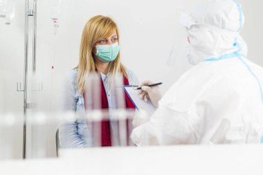 COVID-19 hastanesindeki hastayı muayene eden sağlık çalışanı. Coronavirus için PCR teşhisi. PPE 'deki doktor hastalara semptomlar yazıyor..