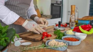 Mutfaktaki ahşap bir tahtanın üzerinde hamburgerler için et şekillendiren bir şefin yakın çekimi. Çeşitli baharatlar, sebzeler ve iş yüzeyinin etrafında küçük mutfak kaseleri var..