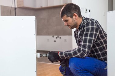 Mutfak raflarında önceden belirlenmiş bir yere yerleştirmeden önce dairesel matkapla delik açan bir marangoz..