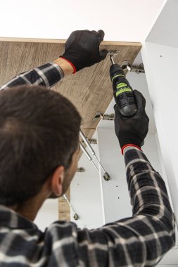 Marangoz mutfak raf kapısının mekanizmalarını (eklemlerini) kurar ve vidalar.