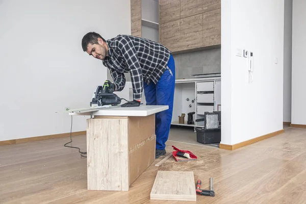 部屋の床に木製の板を切る大工 彼は自分の仕事を木箱の上で実行し それは彼に仕事のテーブルとして役立ちました — ストック写真
